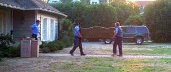 A couple of movers carry a couch toward the house